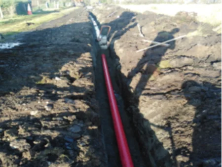 A construction site for the Black Lough Wind Farm project, featuring a long dug trench with a red pipe being lined up to carry cables