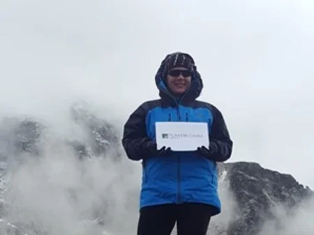 Grainne Rouleau standing and holding white paper with Powercomm logo on top of Mount Everest.