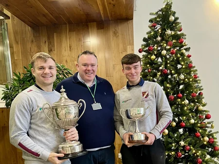 Two employees standing on either side of James Cafferty each holding a Caragh Cup trophy.