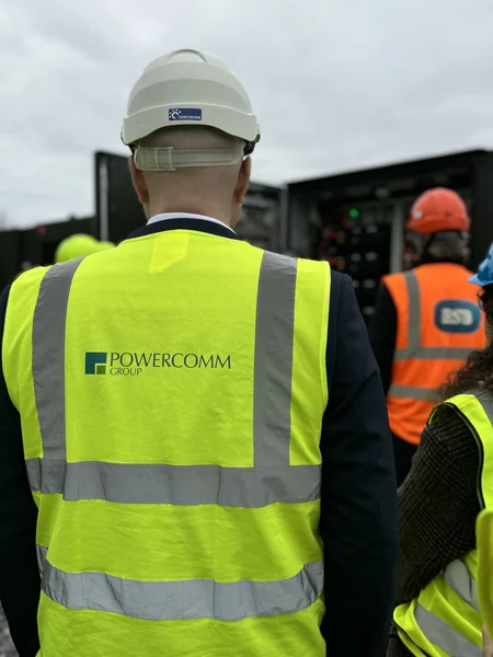 Martin, with his back to the camera, wears a high-vis jacket with the Powercomm logo looking at a Battery Storage solution unit. 