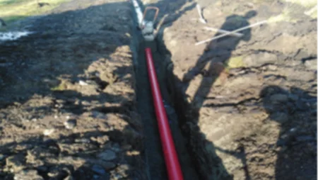 A construction site for the Black Lough Wind Farm project, featuring a long dug trench with a red pipe being lined up to carry cables