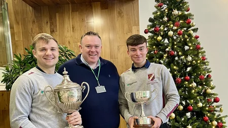 Two employees standing on either side of James Cafferty each holding a Caragh Cup trophy.