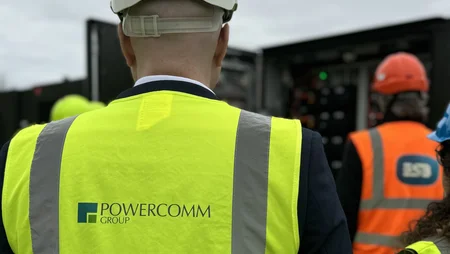 Martin, with his back to the camera, wears a high-vis jacket with the Powercomm logo looking at a Battery Storage solution unit. 